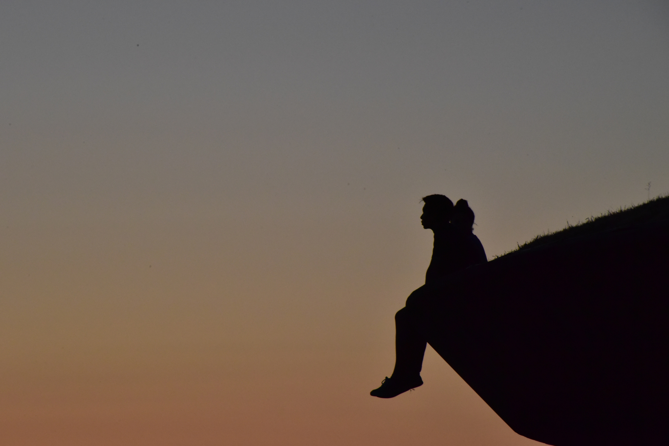 Silhouette of Person Sitting on a Cliff at Dusk